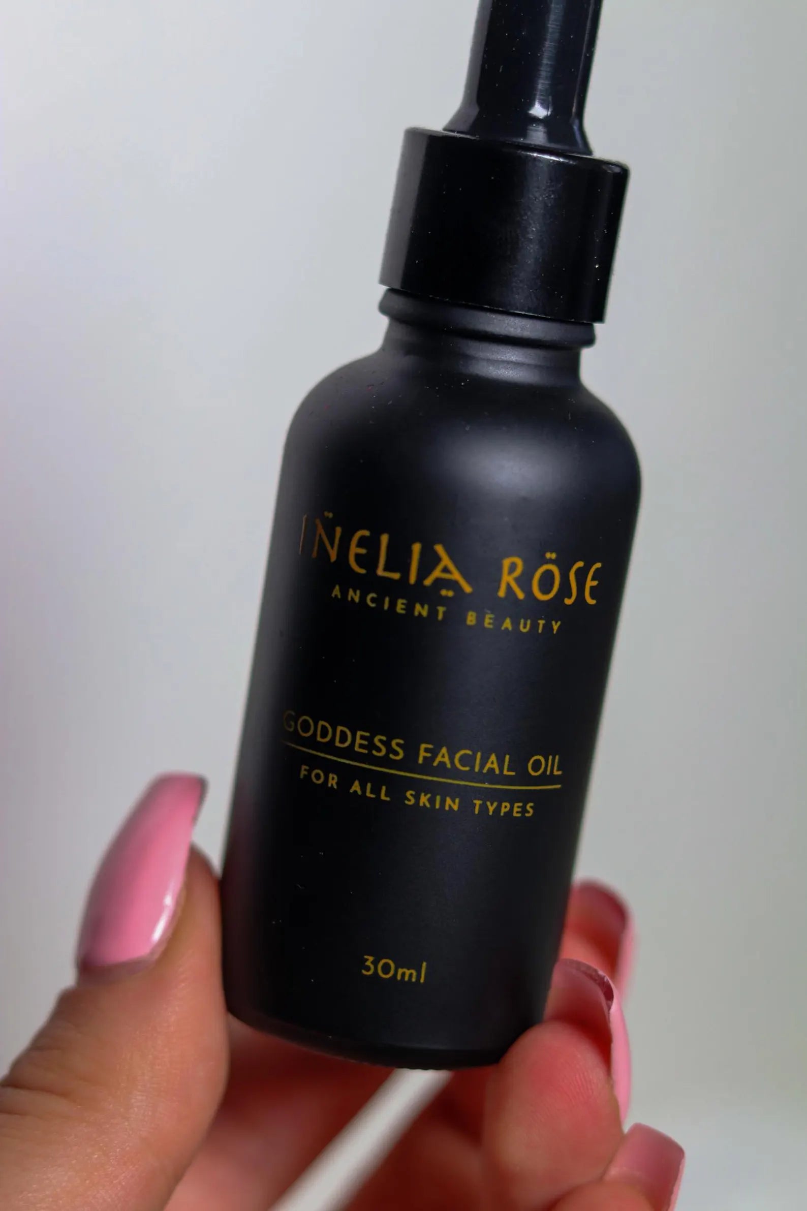 Black facial oil bottle with 'Nelia Rose' branding held by a hand against a plain background